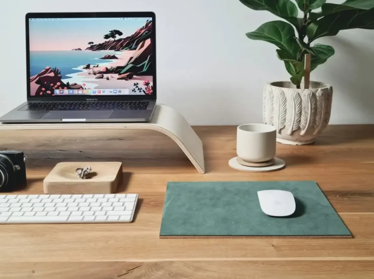Espacio de trabajo minimalista con portátil, teclado, taza de café y planta sobre escritorio de madera.